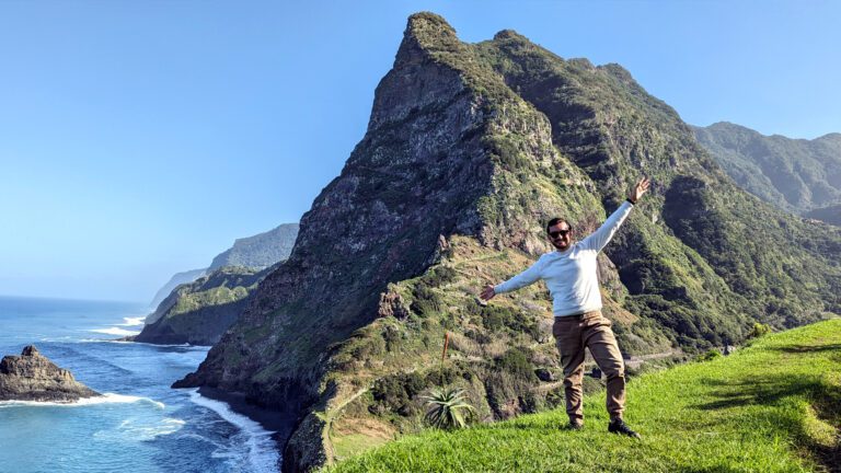 Ross standing with open arms at Miradouro de São Cristóvão with green mountains behind him in warm October light
