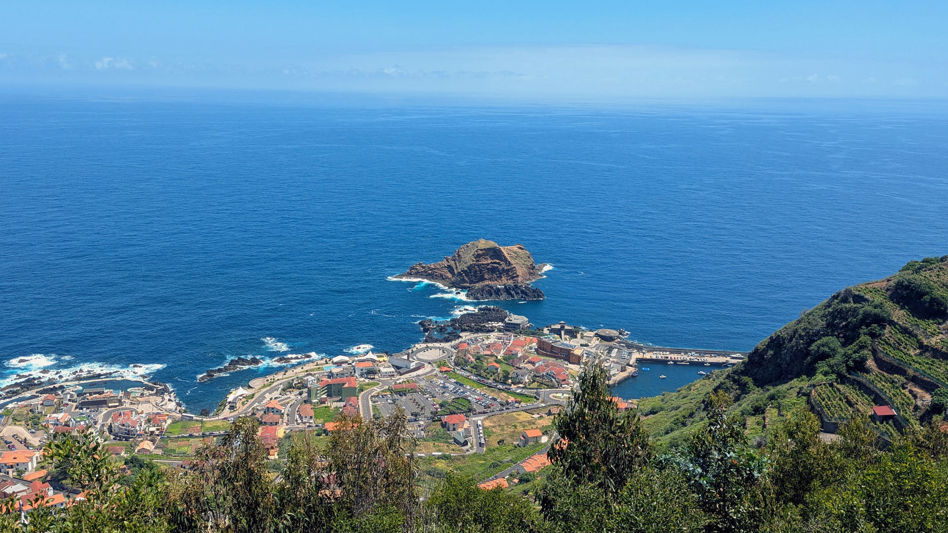 Spring view from Miradouro da Santa with blue sky, calm ocean and Porto Moniz below the cliffs