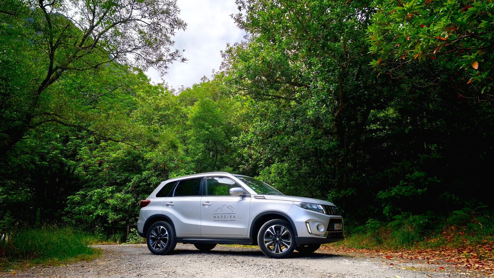 Silver Suzuki Vitara Mild Hybrid parked on an unpaved road surrounded by green Laurissilva forest trees in Chão da Ribeira